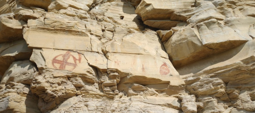 Ancient rock art featuring red symbols on a textured sandstone cliff face.